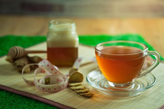 Ginger juice in a clear cup and honey jar placed beside with measuring tape.
Concept of healthy.