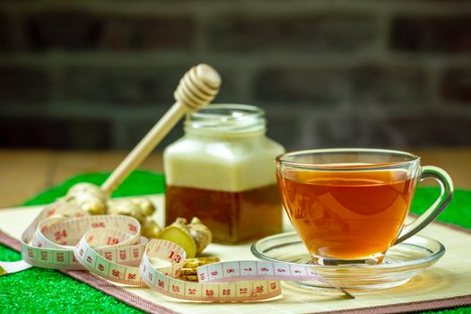 Ginger juice in a clear cup and honey jar placed beside with measuring tape.
Concept of healthy.