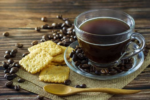 Black coffee in clear glass cup with coffee beans and crackers placed on a hemp mat.