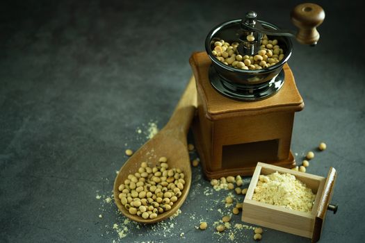 Coffee grinder grinding soybeans into powder and wooden ladle in darkness. Used to make soy milk.