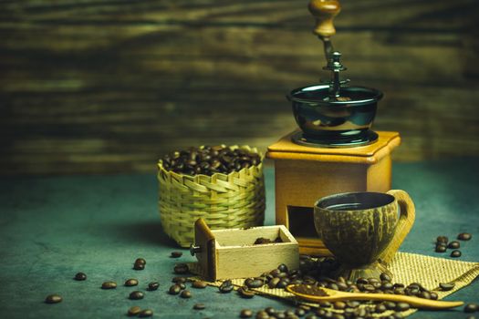 Brew black coffee in coconut cup and morning lighting. Roasted coffee beans in a bamboo basket and wooden spoon. Vintage coffee grinder and moka pot. Concept of coffee time in morning or start the new day.