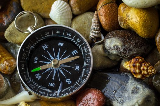 Compass on the pebbles and shell at riverside. Concepts of tourism and adventure.