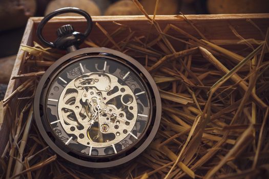 Pocket watch winder on natural wheat straw in a wooden box. Concept of vintage or retro gift.