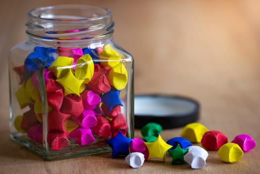 Multicolor paper star in square glass bottle on wooden table with morning sunlight.