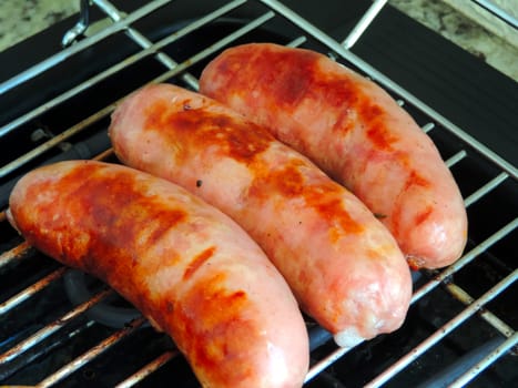 Three grilled sausages on the metal grill