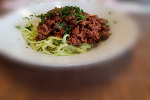 Healthy low carb food on white plate, lunch with snake cucumber in spaghetti strips cut above beef tartare with tomato sauce.