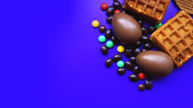 Delicious chocolate easter eggs, waffles, sweets on dark blue background