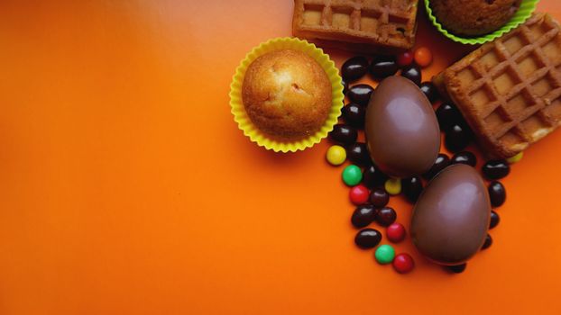 Delicious chocolate easter eggs, waffles, sweets on orange background