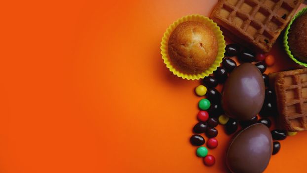 Delicious chocolate easter eggs, waffles, sweets on orange background