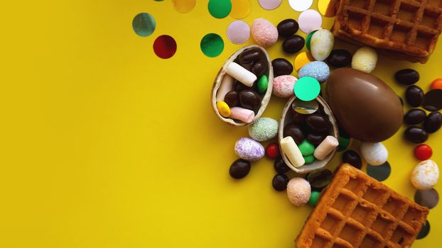 Delicious chocolate easter eggs, waffles, sweets on bright yellow background