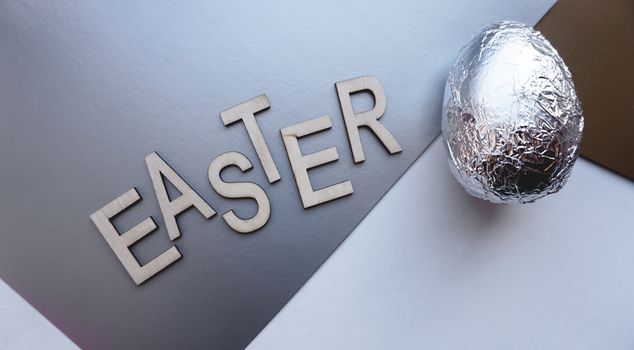 Egg in foil on silver background. Easter concept banner. With text Easter