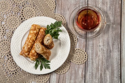 Plate with pancakes with meat and cup of tea on an old wooden background