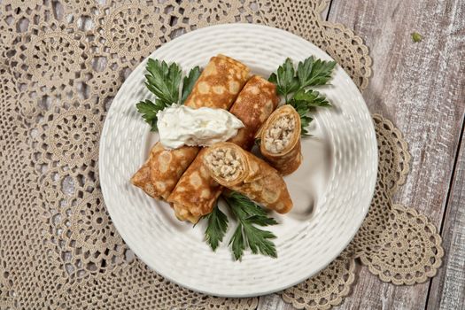 Plate with pancakes with meat and cup of tea on an old wooden background