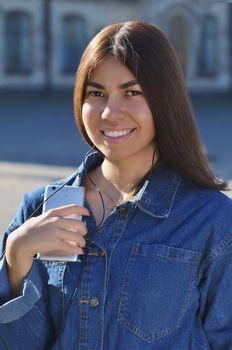 Portrait of a young girl that listens to music, Asian appearance dressed in a denim jacket with a phone in her hands