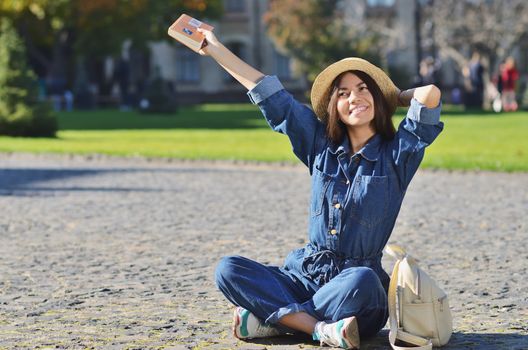 Cheerful young girl of Asian appearance sitting in the campus waving the hand with the book