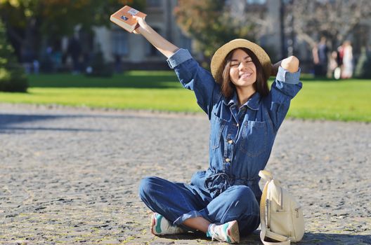 Cheerful young woman is sitting in the campus waving the hand with the book