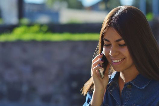 Portrait of a young attractive girl who talks on the phone on the street and smiles