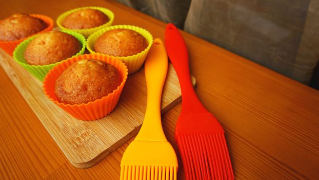 Simple mini muffins in colorful silicone bakeware. Silicone cup baking cupcakes and silicone brushes. Kitchen and cooking concept on wooden background