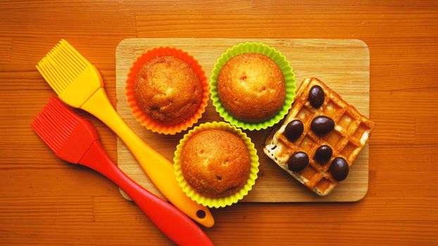 Simple mini muffins in colorful silicone bakeware and waffles. Kitchen and cooking concept on wooden background