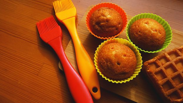 Simple mini muffins in colorful silicone bakeware. Silicone cup baking cupcakes and silicone brushes. Kitchen and cooking concept on wooden background