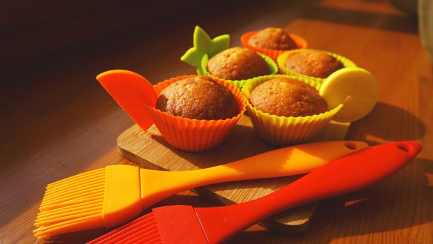 Simple mini muffins in colorful silicone bakeware. Silicone cup baking cupcakes and silicone brushes. Kitchen and cooking concept on wooden background