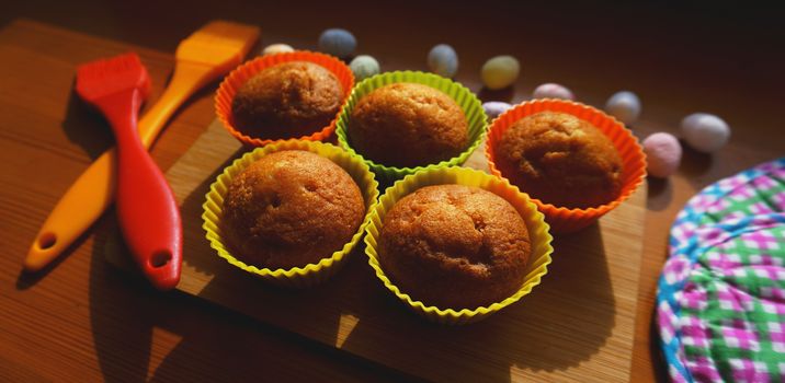 Mini Cakes Decorated with Eggs, Easter Dessert. Simple mini muffins in colorful silicone bakeware. Kitchen and cooking concept on wooden background