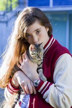 Autumn sunny photo of a teenage girl hugging her cat, close-up, outdoor photo on a blue background