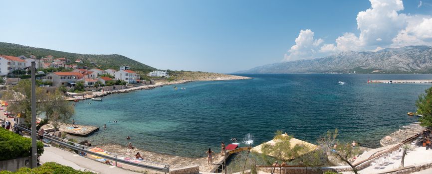 Beach in small village Vinjerac near Zadar, Croatia, people bathing in turquoise blue water in the lagoon and beautiful panorama view on Velebit mountain with Paklenica national park, summer time