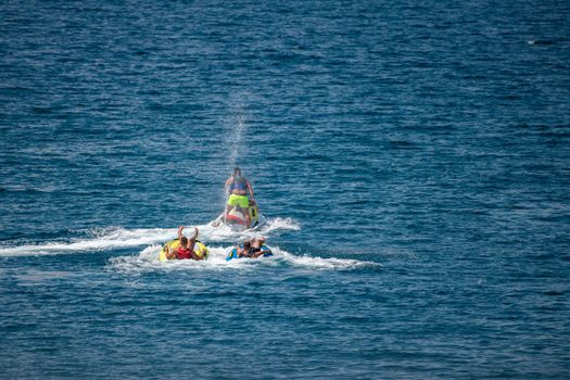 Jet ski pulling two tubes in water, water sports and fun in summer at beach, travel and vacation fun, water spraying all directions