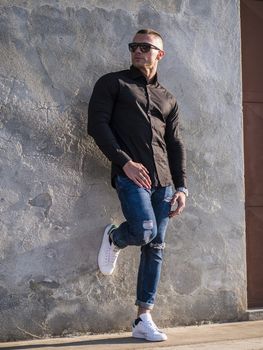 One handsome young man in urban setting in European city, standing, wearing black jacket and jeans