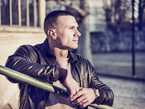 One handsome young man in urban setting in European city, standing, wearing black leather jacket and jeans