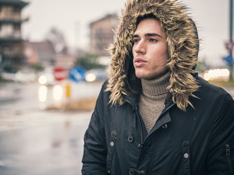 Full length of young man in coat walking under rain along the city street