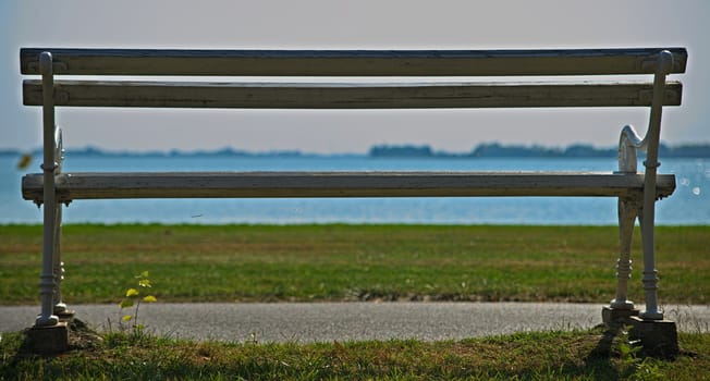 Empty white bench looking at grass field and lake in distance