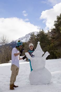 Young boy and girl make a snowman on a sunny day in the winter snow-covered forest in the mountains.