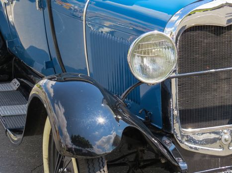 Detail in day of sun, from the classic old car front blue, headlight, radiator and chrome