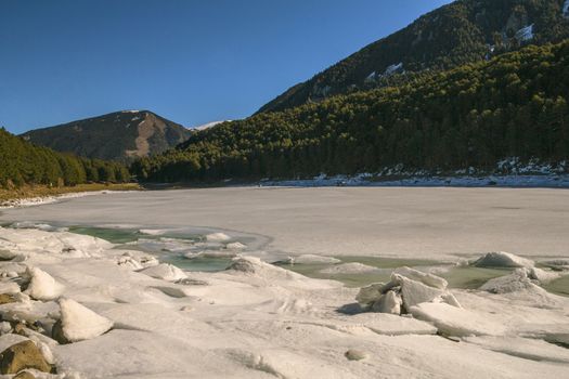 Frozen Lake surrounded by pine trees, with blue sky in Engolasters, Andorra