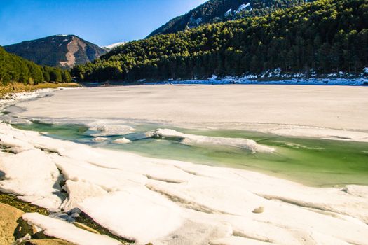 Frozen Lake in Engolasters, Andorra, surrounded by pine trees and with a blue sky