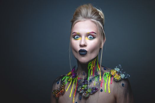 Emotional portrait of a young girl with creative makeup and colorful butterflies on her shoulders