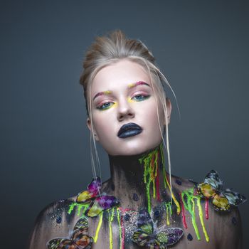 Emotional portrait of a young girl with creative makeup and colorful butterflies on her shoulders