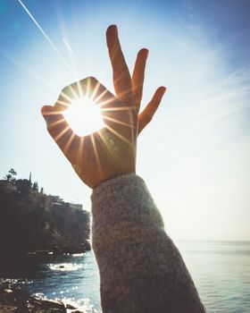 Sun shines through fingers on the shore.