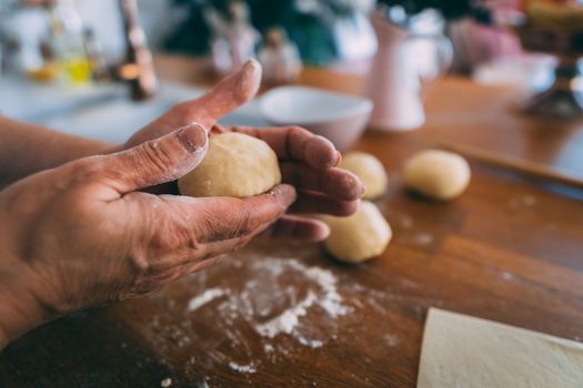 Hands of a woman in the kitchen shaping dough balls.