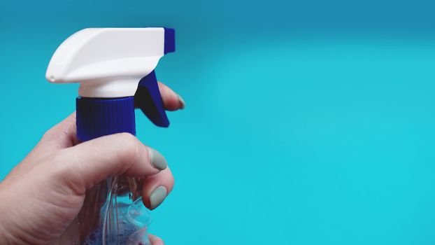 Female hand holding spray with detergent on blue background. Housework, housekeeping and household concept