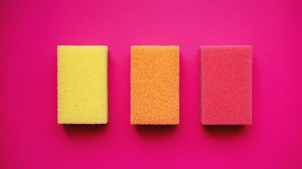 Sponges - top view. Household cleaning concept. Colorful orange pink yellow sponges on pink background.