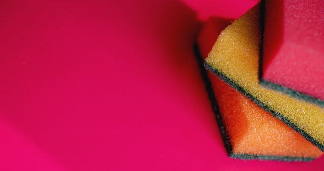 Sponges - close-up. Household cleaning concept. Colorful orange pink yellow sponges on pink background, soft focus, copy text.