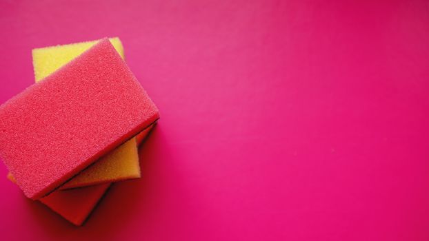 Sponges - close-up. Household cleaning concept. Colorful orange pink yellow sponges on pink background, soft focus, copy text.