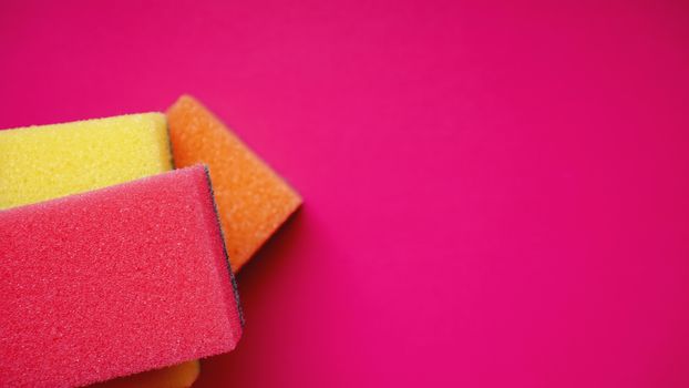 Sponges - close-up. Household cleaning concept. Colorful orange pink yellow sponges on pink background, soft focus, copy text.