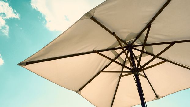 White fabric color texture beach umbrella and brown wood tripod with white cloud and clear blue sky summer sunlight day in low angle view camera for travel asia Thailand Pattaya.