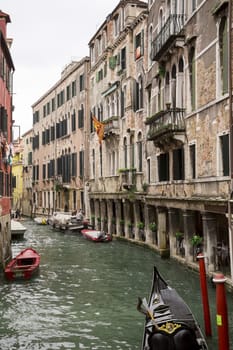 Venetian canal with a variety of boats moored to old Italian buildings with peeling walls.