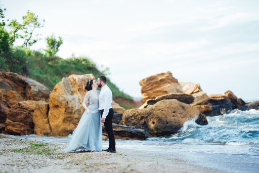 same couple with a bride in a blue dress walk along the ocean shore