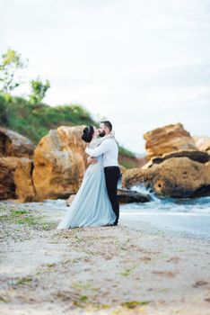 same couple with a bride in a blue dress walk along the ocean shore